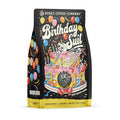 The front of a 12 ounce bag of Bones Coffee Company Birthday Suit coffee. Its flavor is birthday cake, and it has a skeleton laying on a birthday cake with a birthday hat on blowing into a streamer on the front.
