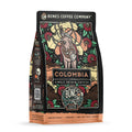 The front of a 12 ounce bag of Bones Coffee Company Colombia single-origin coffee. It is a medium roast, and it has a donkey with bags of coffee on its back and flowers around it on the art.