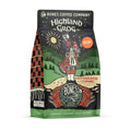 The front of a 12 ounce bag of Bones Coffee Company Highland Grog decaf coffee. Its flavor is caramel and butterscotch, and it has a skeleton wearing a kilt playing bagpipes on a hill on the art.