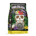 The front of a 12 ounce bag of Bones Coffee Company Pina Colada flavored coffee. It is pineapple and coconut flavored, and It has a skeleton cup with a straw, bits of pineapple and coconut, and an umbrella inside it on the art. 