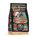 The front of a 12 ounce bag of Bones Coffee Company Toffee Almond Crunch coffee. Its flavor is toffee almond crunch, and it has a skeleton dressed up for christmas holding a basket of toffee almond crunch with a skeletal cat on the art.