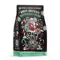 The front of a 12 ounce bag of Bones Coffee Company White Chocolate Peppermint Bark coffee. Its flavor is white chocolate peppermint bark. It has skeletons dressed as Santa in a peppermint cane field on the art.