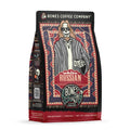 The front of a 12 ounce bag of Bones Coffee Company White Russian coffee. Its flavor is cream and coffee liqueur, and it has a skeleton wearing sunglasses with a goatee in a comfy coat with a white tee shirt holding a cup of coffee on the art.