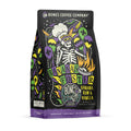 The front of a 12 ounce bag of Bones Coffee Company Bananas Foster coffee. Its flavor is banana, rum, and vanilla, and it has a skeleton wearing a chef’s hat and mardi gras glasses with balloons with the New Orleans emblem on the art.