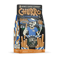 The front of a 12 ounce bag of Bones Coffee Company Churro coffee. Its flavor is churro, and it has a skeleton in front of a churro stand holding out churros on the art.