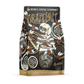The front of a 12 ounce bag of Bones Coffee Company Crazelnut flavored coffee. It is hazelnut flavored, and it has a skeleton with crazy eyes and a cracked skull eating hazelnuts with other hazelnuts flying around on the art. 