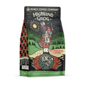 The front of a 12 ounce bag of Bones Coffee Company Highland Grog coffee. Its flavor is caramel and butterscotch, and it has a skeleton wearing a kilt playing bagpipes on a hill on the art.