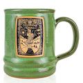 The front of the Bones Coffee Company Irish Cream Handthrown Mug. It has the Irish Cream art on the golden medallion. The mug is jade colored.