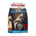 The front of a 12 ounce bag of Bones Coffee Company Megalodonut flavored coffee. It is boston cream donut flavored, and it has a skeleton fishing from a boat using a donut as bait as a donut shark goes to bite the line on the art. 