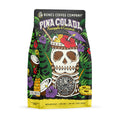 The front of a 12 ounce bag of Bones Coffee Company Pina Colada flavored coffee. It is pineapple and coconut flavored, and It has a skeleton cup with a straw, bits of pineapple and coconut, and an umbrella inside it on the art. 